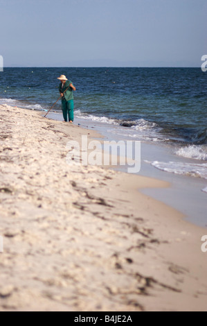 Hotel Gärtner mit einer grünen Uniform und einen Strohhut Rechen einen Sandstrand am Mittelmeer in Tunesien. Stockfoto