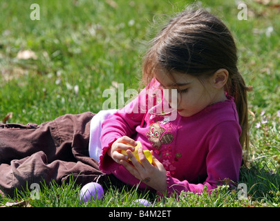 Ein hübsches kleines Mädchen, fünf Jahre alt, liegt in der Wiese an einem sonnigen Nachmittag Kommissionierung durch die Ostereier, die sie gefunden wird. Stockfoto