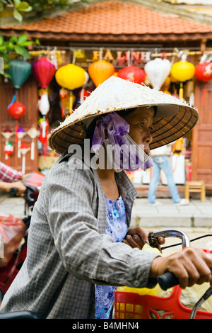 Vietnamesin mit Fahrrad und Geschäft mit chinesischen Laternen im Hintergrund; Hoi an, Vietnam Stockfoto