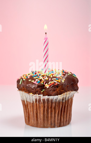 Einen leckeren Muffin Schokolade mit Kerze isoliert auf farbigem Hintergrund Flamme im Fokus und geringe Schärfentiefe Stockfoto