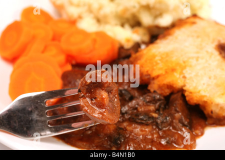 Ein Stück der Lämmer Niere auf einer Gabel ist eine Platte aus Niere und Pilz Talg-Kruste Pie mit Möhren und Kartoffeln im Hintergrund Stockfoto