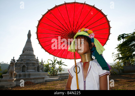 Ein junges Mädchen Longneck posiert vor einem Tempel mit leuchtend roten Sonnenschirm ca. 300 birmanischen Flüchtlinge in Thailand Mitglieder der indigenen Gruppe bekannt sind als die Longnecks, die größte der drei Dörfer wo live Longnecks Nai Soi genannt befindet sich in der Nähe von Mae Hong Son Stadt longnecks, tragen Metallringe auf den Hals, die das Schlüsselbein nach unten drücken und verlängern dem Hals, sie sind, ein Tourist Anziehung Touristen besuchen Nai Soi, fotografieren die Longnecks und kaufen Sie ihr Kunsthandwerk der Dörfer von Menschenrechtsorganisationen als menschliche Zoos kritisiert werden Stockfoto