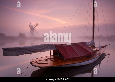 Thurne Windmühle und einem nebligen Fluß Thurne im Morgengrauen auf den Norfolk Broads mit einem traditionellen hölzernen Segelboot im Vordergrund Stockfoto