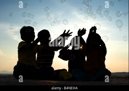 Vier indischen Jungen sitzen auf einem Felsen spielen mit Luftblasen Silhouette. Indien Stockfoto