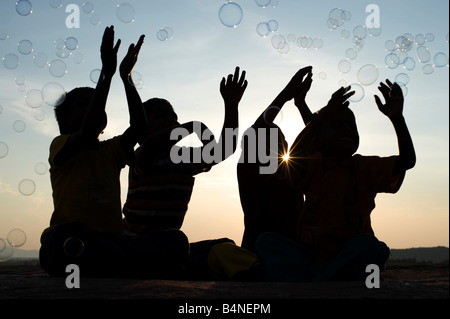 Vier indischen Jungen sitzen auf einem Felsen spielen mit Luftblasen Silhouette. Indien Stockfoto