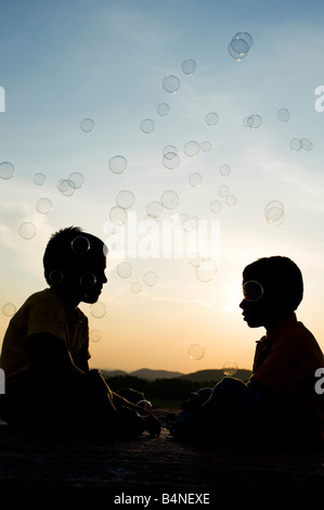 Zwei indische jungen sitzen auf einem Felsen spielen mit Luftblasen Silhouette. Indien Stockfoto