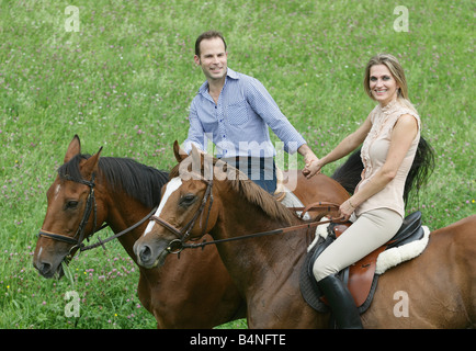 Paar, sitzen auf dem Pferd auf einer grünen Wiese, die Hand in Hand. Stockfoto