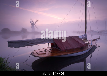 Thurne Windmühle und einem nebligen Fluß Thurne im Morgengrauen auf den Norfolk Broads mit einem traditionellen hölzernen Segelboot im Vordergrund Stockfoto