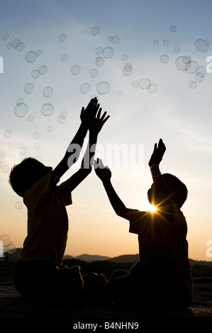 Zwei indische jungen sitzen auf einem Felsen spielen mit Luftblasen Silhouette. Indien Stockfoto