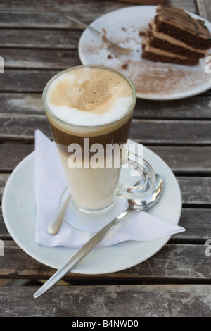 Nahaufnahme eines großen Kaffee Latte mit leckeren Schokoladenkuchen im Hintergrund Stockfoto