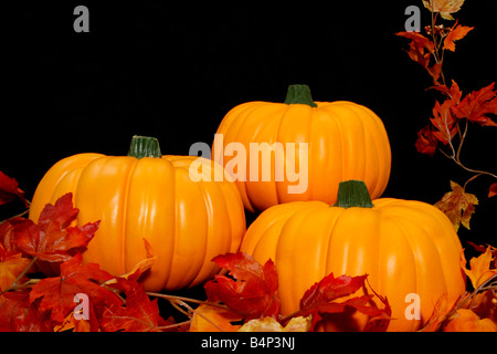 Drei helle orange Kürbisse zusammen angeordnet auf einem schwarzen Hintergrund mit einigen Herbstlaub Stockfoto