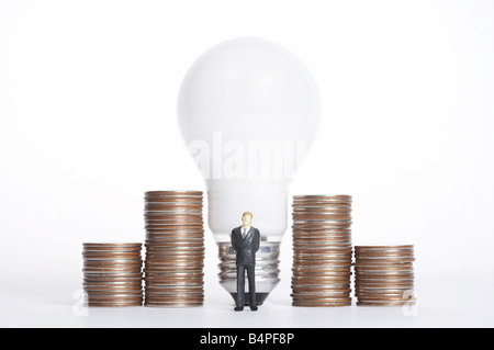 Männliche Figur stand vor Glühbirne und Stapel von Münzen Stockfoto