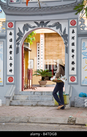 Vietnamesische Dame mit Bambushut, die am Eingang der Pagode vorbeiläuft, Hanoi Vietnam Stockfoto