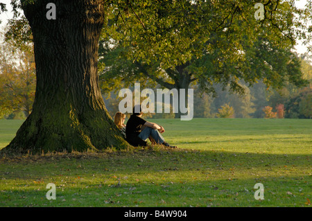 Junges Paar sitzt an den Stamm einer alten Eiche im Herbst, Nonsuch Park, Cheam, (Südwesten von London), Surrey, England Stockfoto