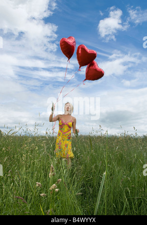 Lächelnde Frau in Feld mit Luftballons Stockfoto