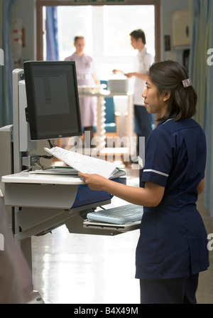 Eine Stationsschwester lächelt, als sie "Kühe", Computer auf Rädern, in eine Akutversorgung Einheit verwendet. Stockfoto