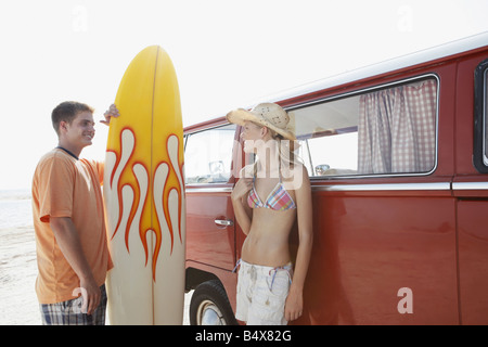 Junges Paar mit Surfbrett stehend mit einem Kleinbus am Strand Stockfoto