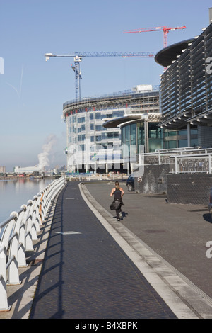 Eine junge Frau joggt entlang Salford Quays neben The Lowry Galleries und eine Contsruction Site Stockfoto