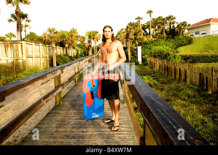Ein langhaariger junger Mann mit einem Boogie Board auf der Promenade am Strand von Ponte Vedra Beach, Florida Stockfoto