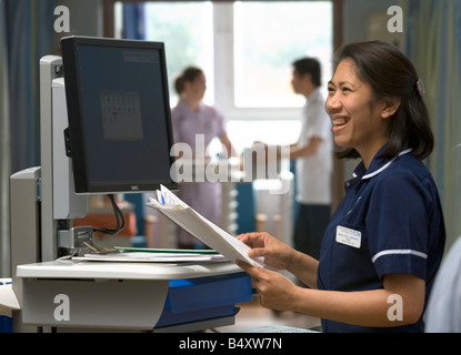 Eine Stationsschwester lächelt, als sie "Kühe", Computer auf Rädern, in eine Akutversorgung Einheit verwendet. Stockfoto