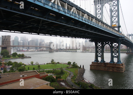 Manhattan Bridge, die die Brooklyn Bridge und Manhattan im Hintergrund umrahmt. Im Vordergrund steht Empire Fulton Ferry Park, Brooklyn, New York City. Stockfoto