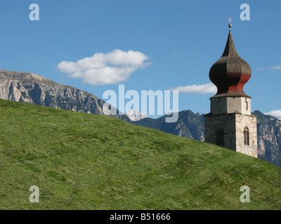Turm der Kirche hinter einer Wiese mit Bergen im Hintergrund, Südtirol, Italien Stockfoto