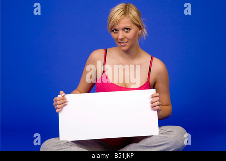 Schwangere Frau Woth gekreuzt Beinen auf dem Boden sitzt und ein weißes Schild in den Händen hält Stockfoto