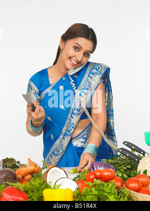 asiatische Frau Schneiden von Gemüse und sprechen in das Telefon Stockfoto