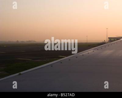 Blick auf eine Flugzeugtragfläche in den Sonnenuntergang am Amsterdamer Flughafen Schiphol Stockfoto