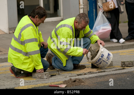 Zwei Kommunalbeschäftigten Reparatur Pflaster tragen hell gelb Warnschutz Jacken kniete, UK Stockfoto