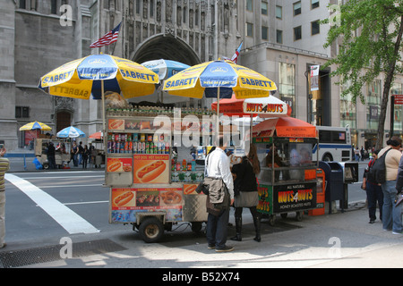 Leute, die eine Brezel von einem Hot Dog Händler in Midtown Manhattan kaufen. Neben ihnen ist ein Verkäufer, der kandierte Nüsse verkauft. New York, 4. Mai 2008 Stockfoto