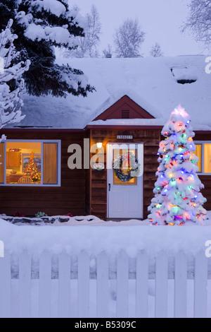 Einfamilienhaus mit Schnee bedeckt mit einem beleuchteten Weihnachtsbaum auf dem Hof in Anchorage, Alaska Stockfoto