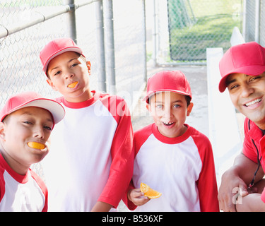 Multi-ethnischen jungen in Baseball Uniformen und Trainer in Essen Orangen Einbaum Stockfoto