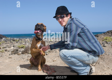 junger Erwachsener Mann mit Hund am Strand mit blauem Himmel Stockfoto