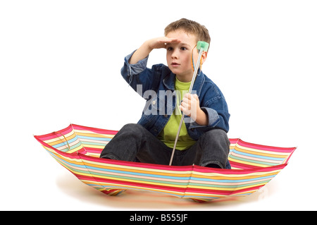 Sieben Jahre alter Junge sitzt in einem Regenschirm spielen wie es s ein Boot Stockfoto