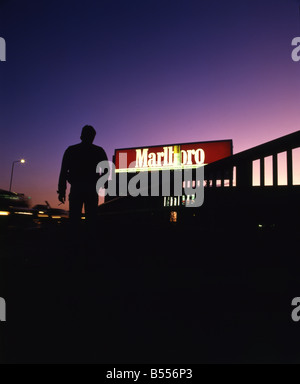 Silhouette eines Mannes mit einer Zigarette zu Fuß in Richtung einer Marlboro beleuchteten Werbetafel Stockfoto