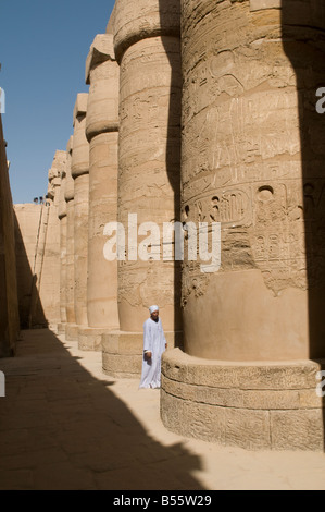 Ein ägyptischer Mann steht inmitten einer geschnitzten Säulen der großen Säulenhalle aus dem Revier des Amun-Re, Karnak Tempel in der Nähe von Luxor Ägypten Komplex Stockfoto