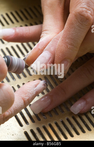Die Gestaltung der falschen Fingernägel mit einem kleinen Rad. Façonnage de faux Ongles Avec Une petite Meule. Stockfoto