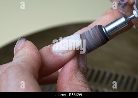 Die Gestaltung der falschen Fingernägel mit einem kleinen Rad. Le Façonnage de faux Ongles Avec Une petite Meule. Stockfoto