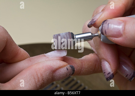 Die Gestaltung der falschen Fingernägel mit einem kleinen Rad. Façonnage de faux Ongles Avec Une petite Meule. Stockfoto