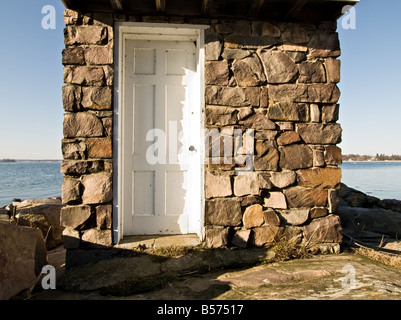 Ein kleines Steinhaus mit einer weißen Tür direkt am Wasser Stockfoto