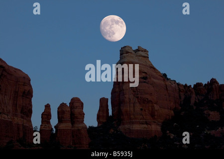 fast Vollmond steigt über roten Felsen Türme in der Nähe von Sedona Arizona Stockfoto