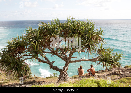 Zwei junge Männer Leute sitzen unter Pandanus Palmen Blick aufs Meer Gorge Walk North Stradbroke Island Queensland QLD Australien Stockfoto