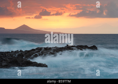 Wellen brechen über Felsen am El Confital auf Gran Canaria. Pico de Galdar Mount Teide auf Teneriffa Oon rechts und links Stockfoto