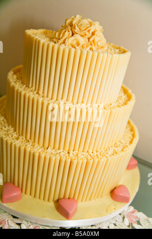 Dreistöckige Hochzeitstorte aus weißer Schokolade, verziert mit Glasrosen und rosa Schokoladenherzen. Stockfoto