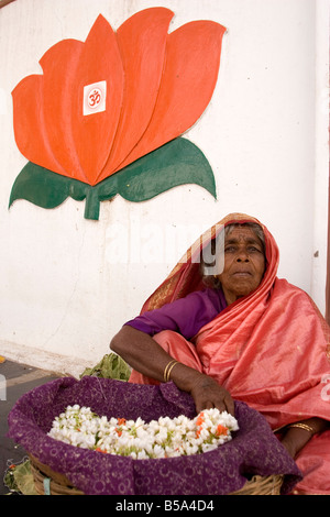 Frauen verkaufen Blumen in Mysore, Indien. Ein roter Lotus mit dem Om-Symbol drauf ist an der Wand über hier. Stockfoto