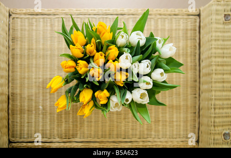 Eine Vase mit weißen Rosen und gelben Lilien auf ein Glas und Wicker Tisch von oben geschossen. Stockfoto