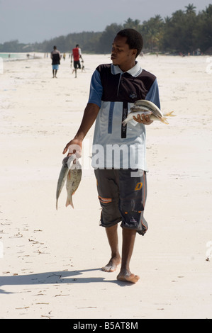 Ein Mann zu Fuß entlang des Strandes mit seinem Fang des Tages Jambiani Sansibar Tansania Ostafrika Afrika Stockfoto