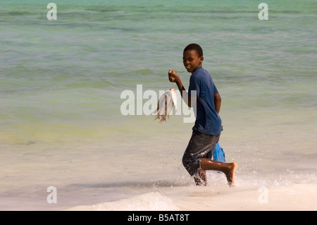 Ein Junge läuft in das Meer mit seinem kürzlich gefangenen Fisch in der hand Jambiani Sansibar Tansania Ostafrika Afrika Stockfoto