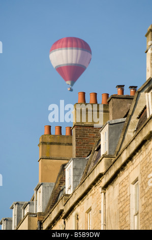 Ein roter und weißer Heißluftballon fliegt über die Dächer von Bad in Südengland Stockfoto